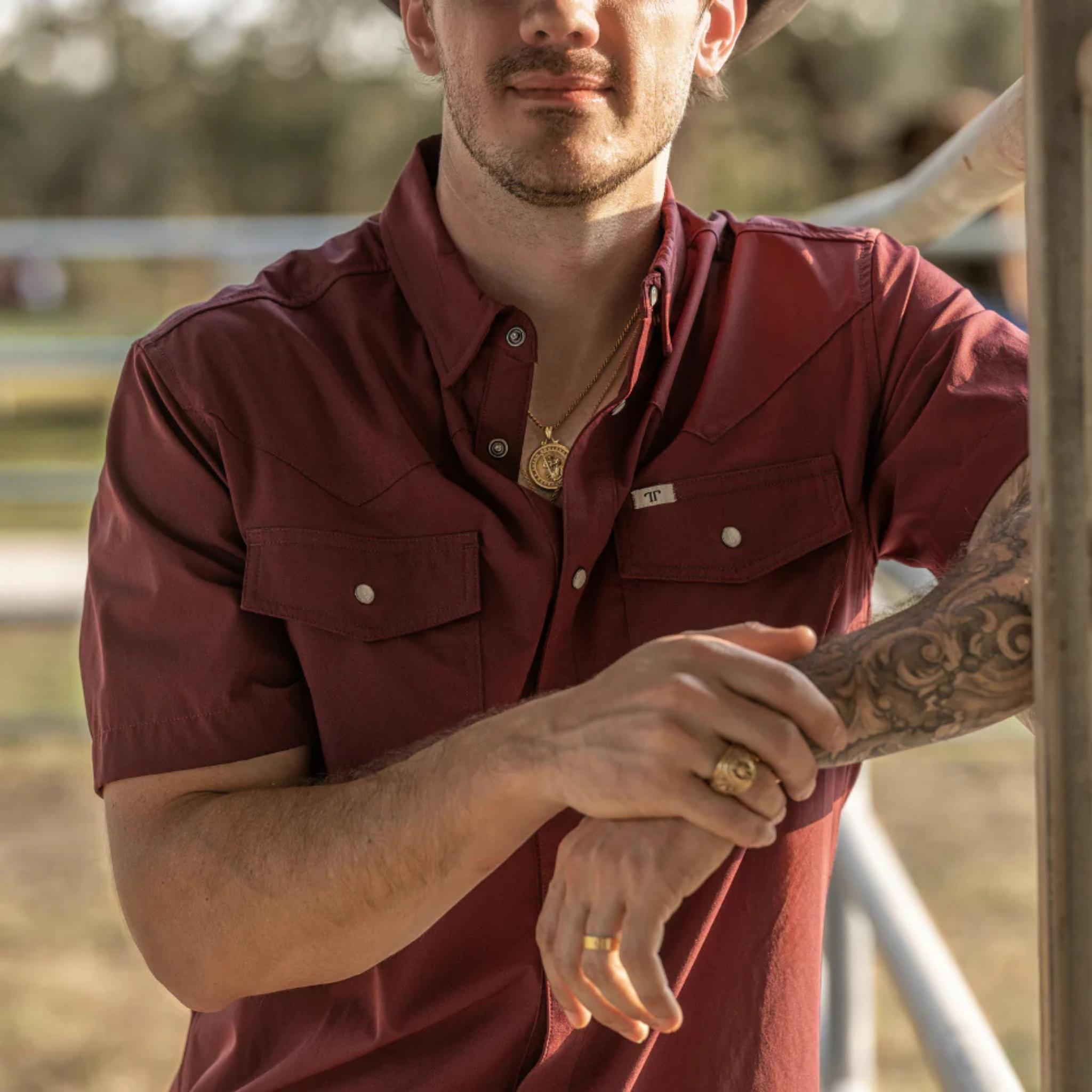 Man wearing a maroon shirt with a blurred outdoor background