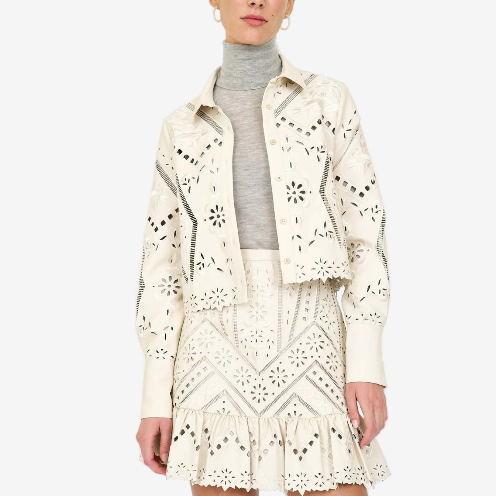 Cream‑colored laser‑cut jacket with floral and geometric cutout patterns, paired with a matching high‑waisted mini skirt with a ruffled hem, worn over a light gray turtleneck.