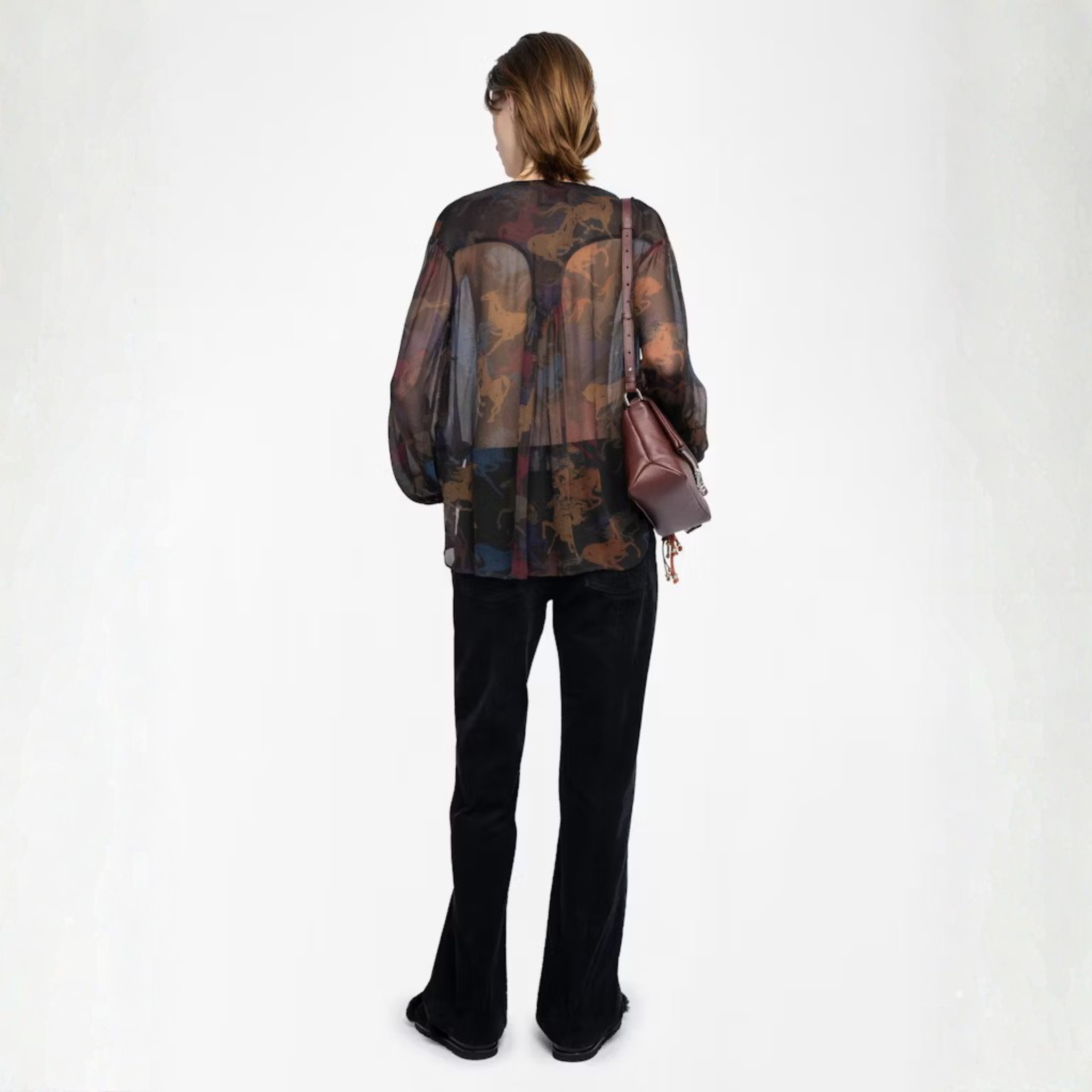 Back view of a person wearing a patterned top and black pants with a brown bag on a white background