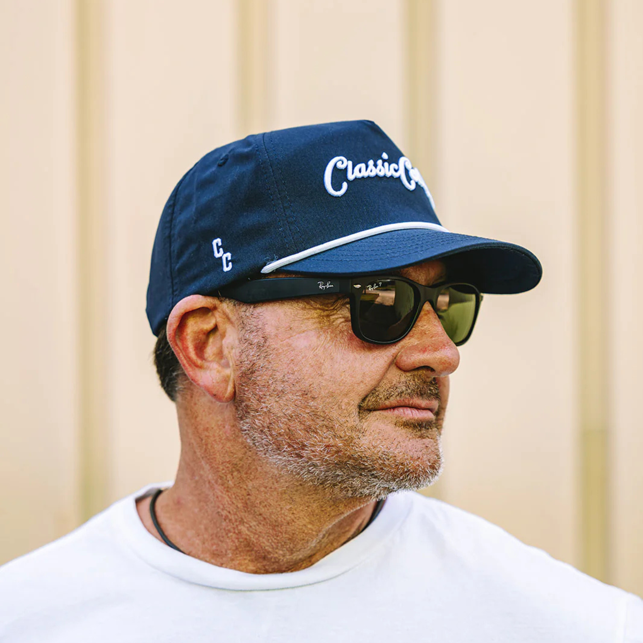 Man wearing a blue cap with 'Classic Cowboy' logo and sunglasses against a beige background